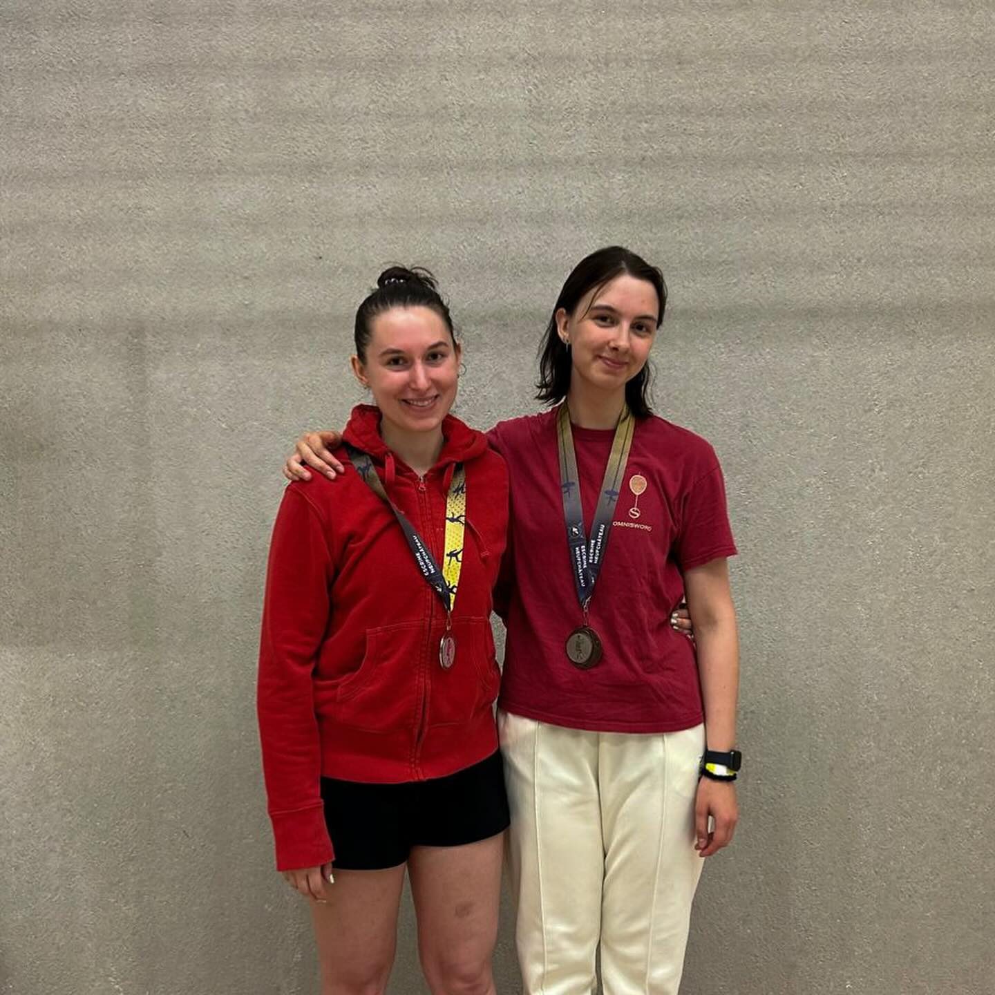 Twee schermsters van de club naast elkaar in clubkleuren, met hun medaille om.